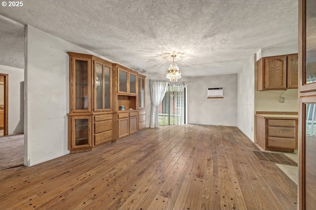 unfurnished living room featuring a wall unit AC, hardwood / wood-style flooring, a chandelier, and a textured ceiling