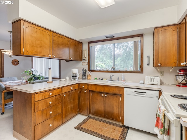 kitchen featuring white appliances, a sink, a peninsula, light countertops, and brown cabinets