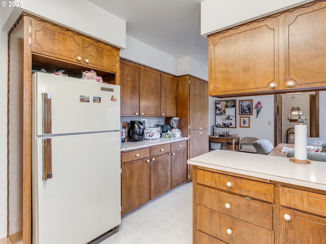 kitchen featuring freestanding refrigerator, light countertops, brown cabinets, light flooring, and a desk