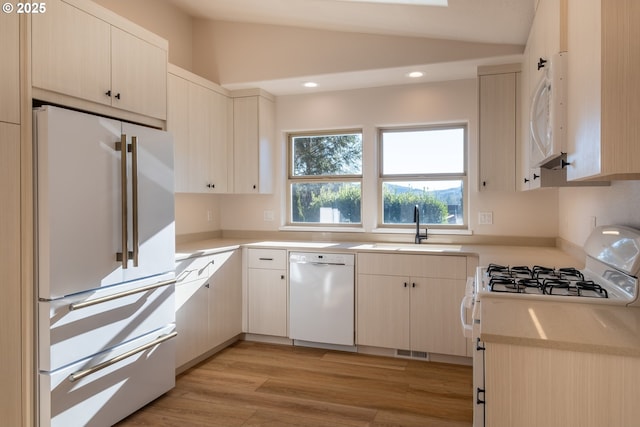 kitchen featuring vaulted ceiling, white appliances, sink, and light wood-type flooring