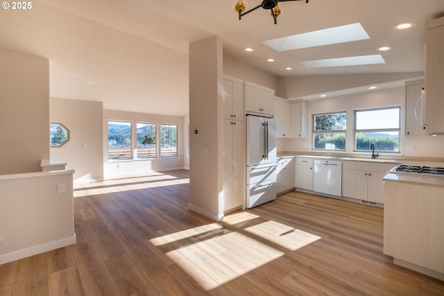 kitchen with sink, vaulted ceiling with skylight, white cabinets, and white appliances