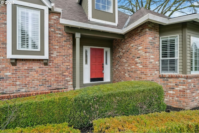 view of exterior entry featuring roof with shingles and brick siding