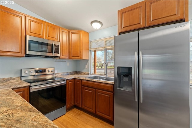 kitchen featuring light hardwood / wood-style floors, light stone countertops, appliances with stainless steel finishes, sink, and lofted ceiling