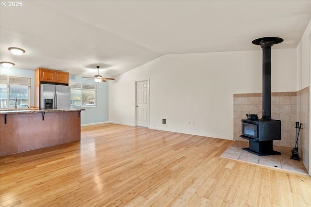 unfurnished living room featuring light wood-type flooring, a wood stove, ceiling fan, and vaulted ceiling