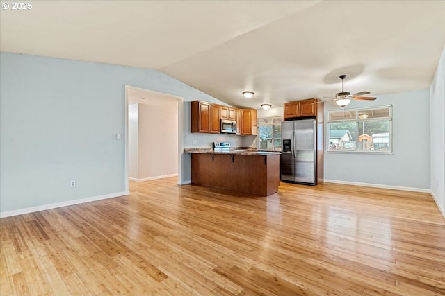 kitchen featuring appliances with stainless steel finishes, lofted ceiling, ceiling fan, light hardwood / wood-style flooring, and a breakfast bar area