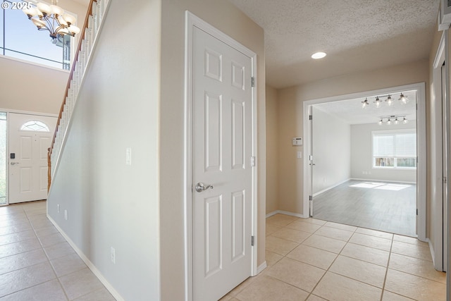 corridor featuring baseboards, stairway, light tile patterned floors, an inviting chandelier, and a textured ceiling