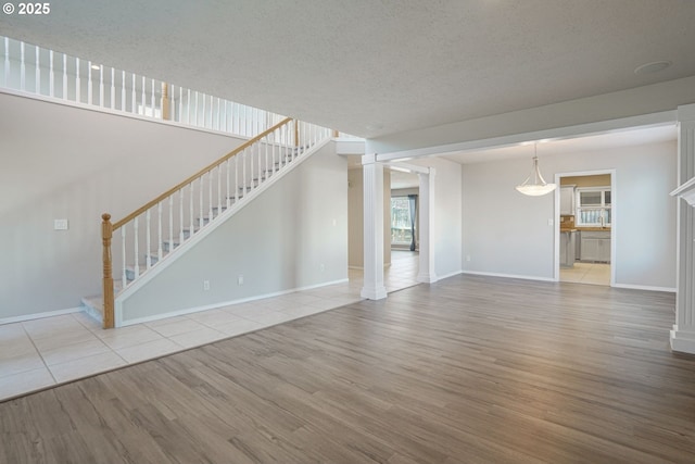 unfurnished living room with baseboards, stairway, decorative columns, wood finished floors, and a textured ceiling