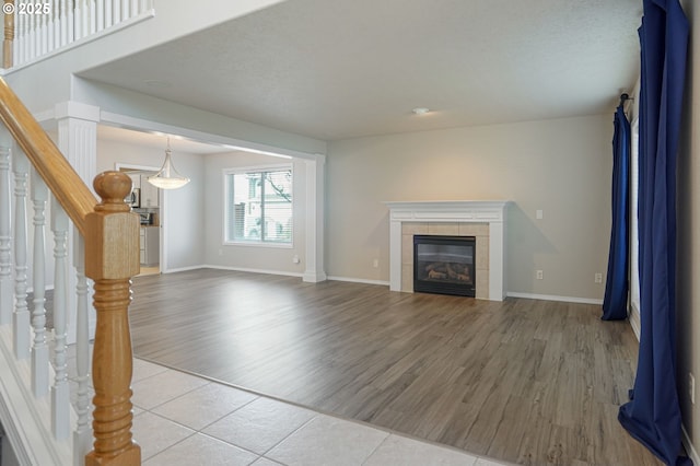 unfurnished living room featuring a tiled fireplace, stairway, light wood-type flooring, and baseboards