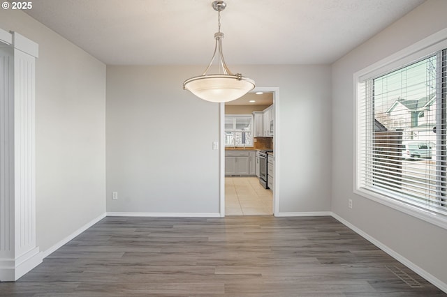 unfurnished dining area with a healthy amount of sunlight, light wood-type flooring, baseboards, and a sink