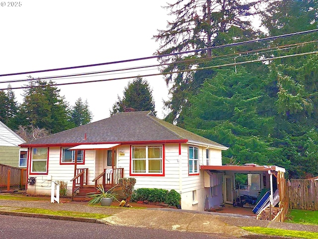 bungalow-style home with a shingled roof, fence, and a carport