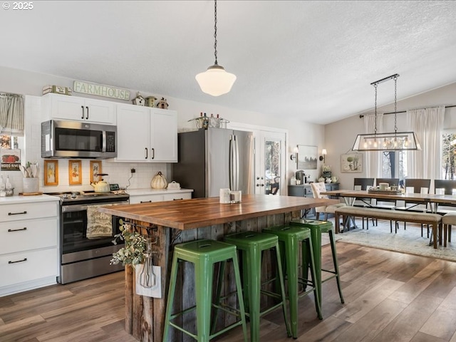 kitchen featuring stainless steel appliances, wood counters, white cabinets, a center island, and pendant lighting