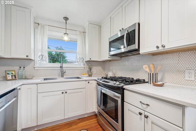kitchen featuring appliances with stainless steel finishes, a sink, tasteful backsplash, white cabinets, and hanging light fixtures