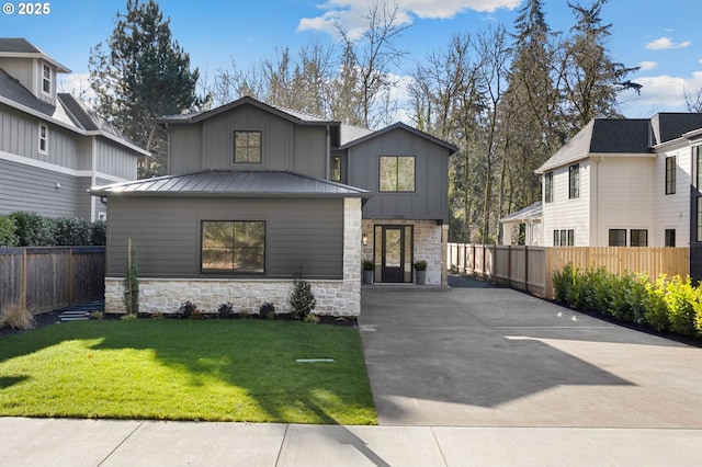 view of front facade featuring concrete driveway, stone siding, a standing seam roof, fence, and board and batten siding