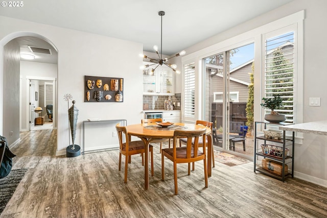 dining space with baseboards, visible vents, arched walkways, wood finished floors, and a notable chandelier