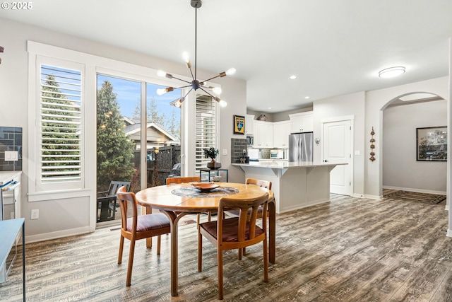 dining area with baseboards, arched walkways, a chandelier, and wood finished floors