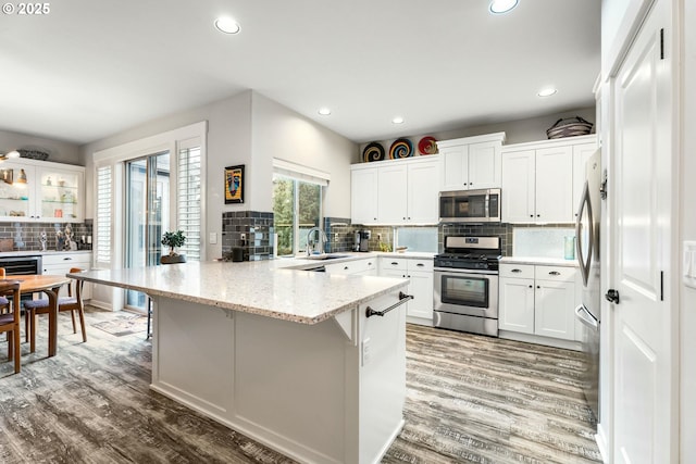 kitchen featuring appliances with stainless steel finishes, white cabinetry, a peninsula, and wood finished floors