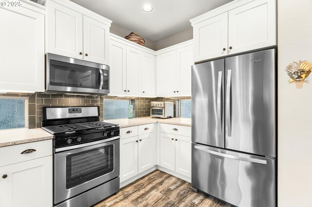 kitchen with tasteful backsplash, appliances with stainless steel finishes, white cabinetry, light stone countertops, and light wood-type flooring