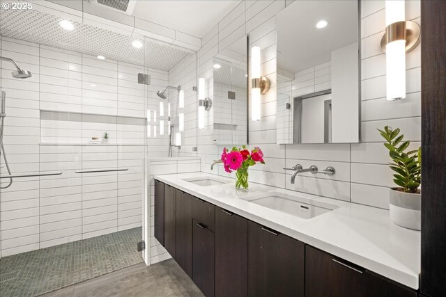 full bath with tiled shower, double vanity, tile walls, and recessed lighting
