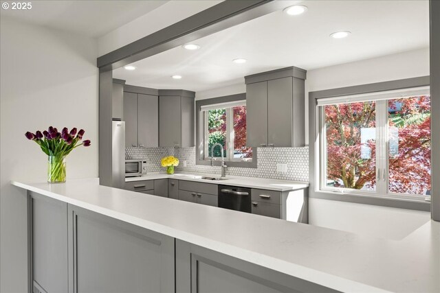 kitchen with gray cabinets, appliances with stainless steel finishes, a sink, tasteful backsplash, and light countertops