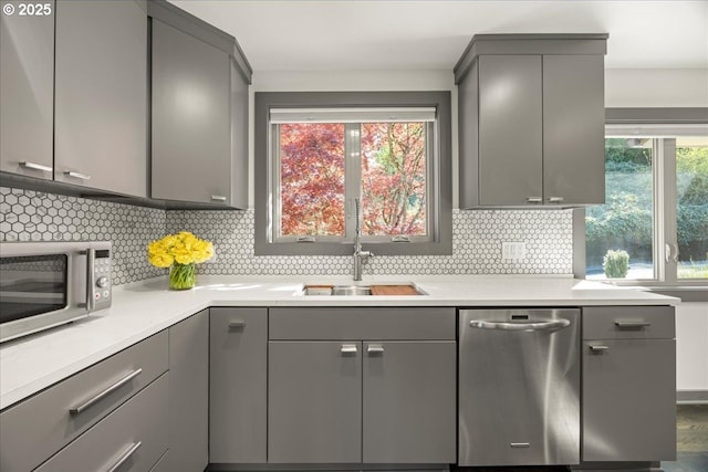 kitchen featuring gray cabinetry, appliances with stainless steel finishes, a sink, and decorative backsplash