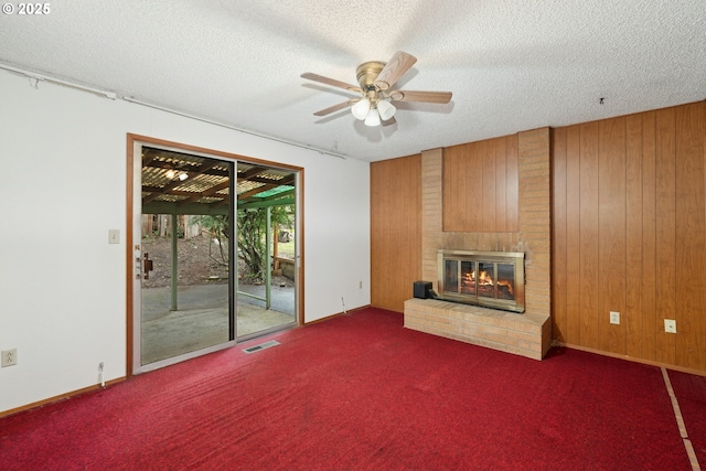 unfurnished living room featuring dark colored carpet, a brick fireplace, and wooden walls