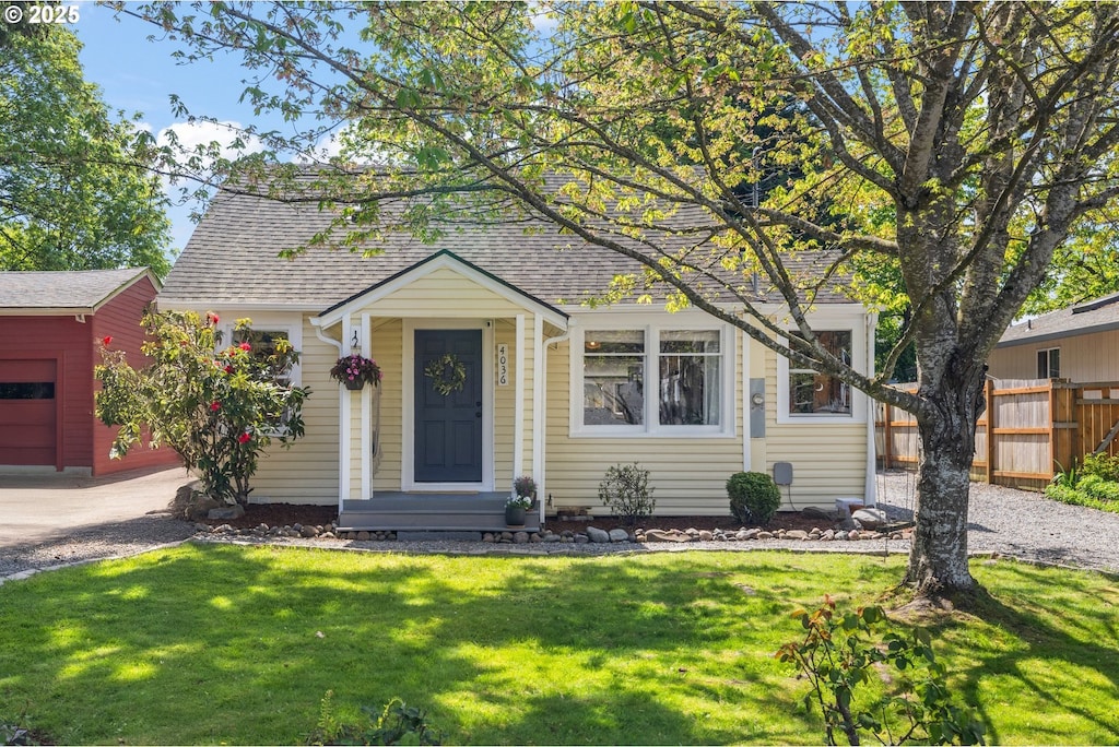 view of front of property featuring fence, a front yard, a shingled roof, and an outbuilding