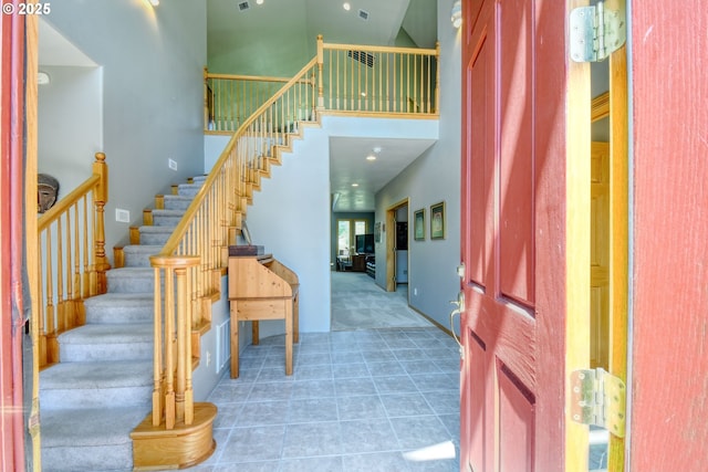 carpeted foyer entrance featuring visible vents, stairs, and a high ceiling