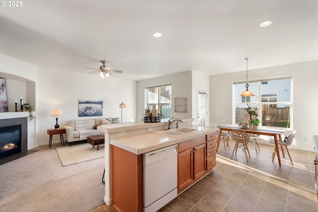 kitchen with brown cabinetry, dishwasher, tile countertops, a fireplace, and a sink