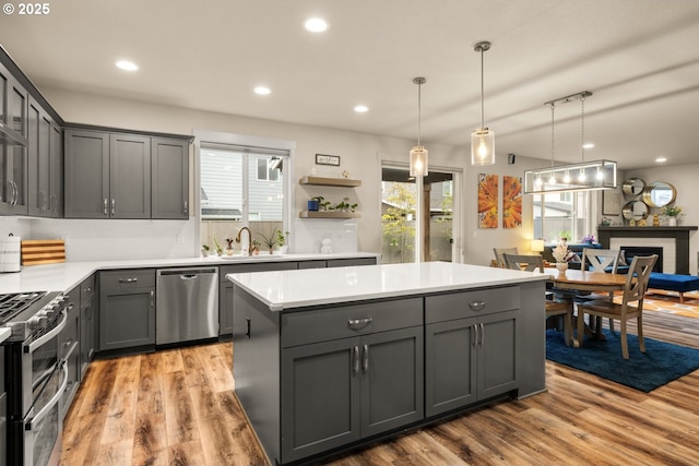 kitchen with gray cabinetry, a sink, light countertops, appliances with stainless steel finishes, and a center island