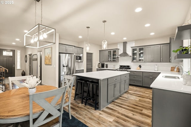 kitchen featuring a center island, stainless steel appliances, gray cabinetry, a sink, and wall chimney range hood