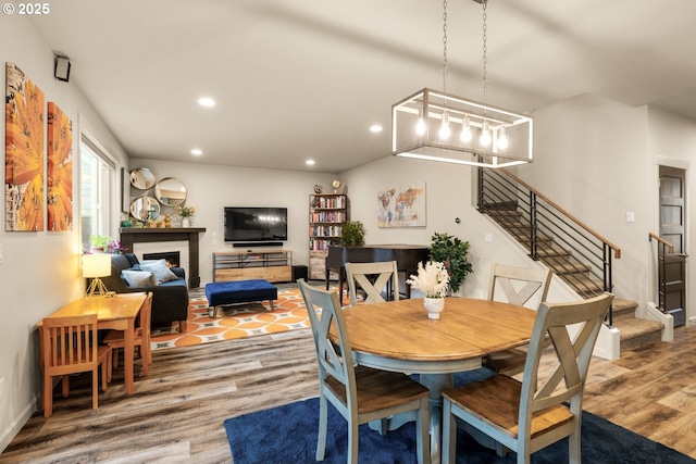 dining space with a warm lit fireplace, stairway, wood finished floors, and recessed lighting