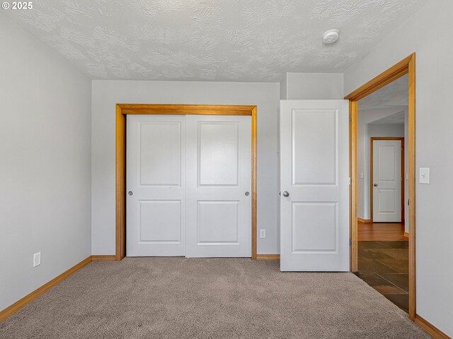 unfurnished bedroom featuring baseboards, carpet flooring, a textured ceiling, and a closet