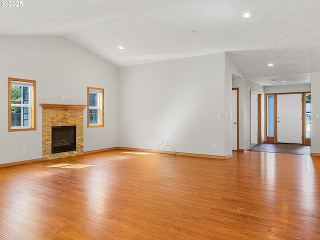 unfurnished living room with wood finished floors, vaulted ceiling, baseboards, recessed lighting, and a glass covered fireplace