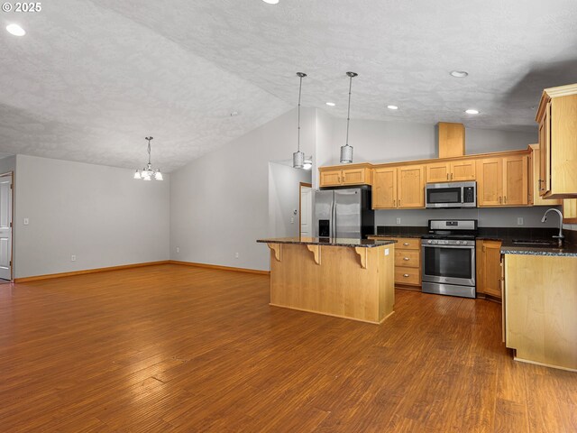 kitchen featuring appliances with stainless steel finishes, lofted ceiling, a sink, a center island, and a kitchen breakfast bar