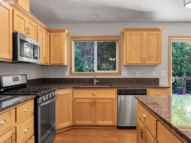 kitchen with stainless steel appliances, a sink, light wood-style floors, dark stone countertops, and a textured ceiling