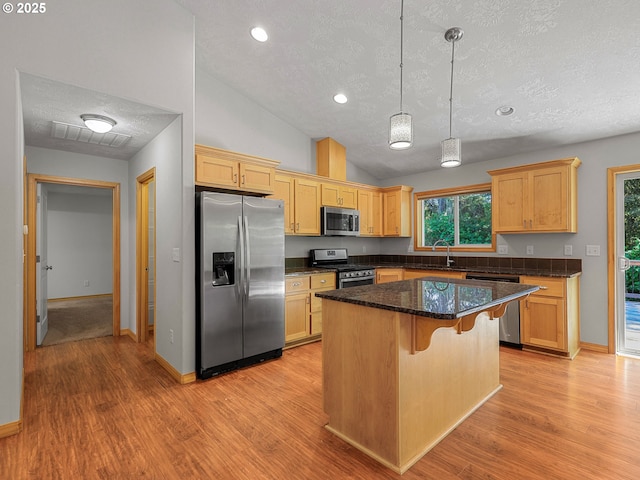 kitchen with stainless steel appliances, a textured ceiling, a kitchen breakfast bar, light wood-style floors, and a kitchen island