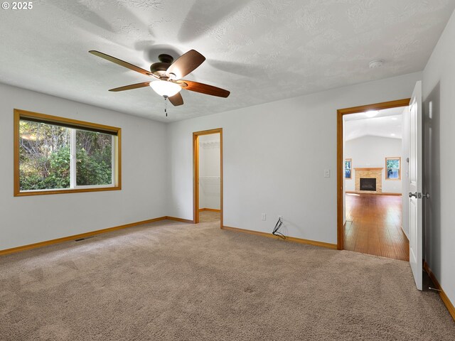 empty room featuring baseboards, a ceiling fan, carpet flooring, a fireplace with raised hearth, and a textured ceiling