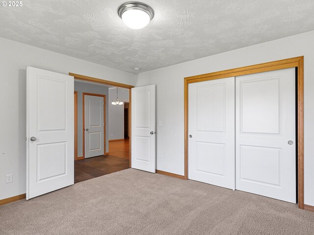 unfurnished bedroom with carpet flooring, baseboards, a textured ceiling, a closet, and a chandelier