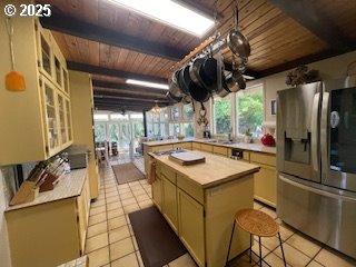 53742 Rosa Rd, Bandon, OR 97411 - kitchen featuring stainless steel refrigerator with ice dispenser, wooden ceiling with exposed beams, light countertops, light tile patterned flooring, and glass insert cabinets
