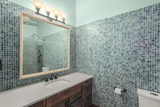 bathroom with a tile shower, vanity, tile walls, and toilet