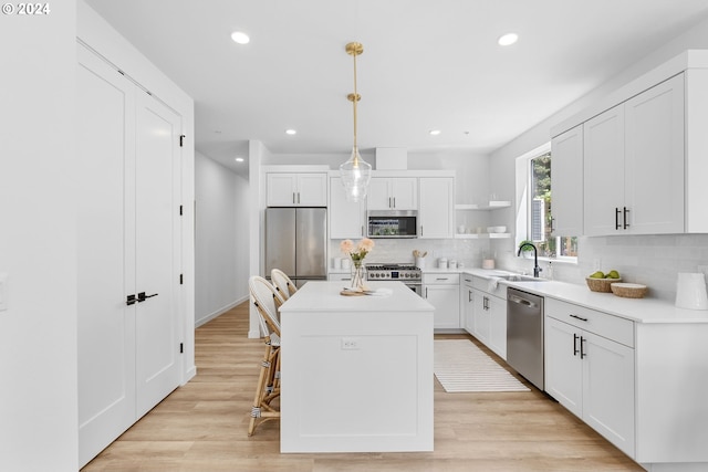 kitchen featuring appliances with stainless steel finishes, sink, decorative light fixtures, white cabinets, and a kitchen island