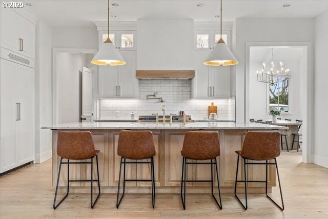 kitchen with decorative backsplash, a kitchen island with sink, light wood-type flooring, and pendant lighting