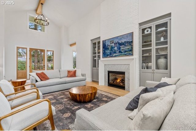 living area with a chandelier, wood finished floors, beam ceiling, a high end fireplace, and high vaulted ceiling