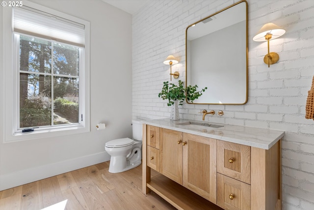 bathroom with healthy amount of natural light, wood finished floors, baseboards, toilet, and brick wall