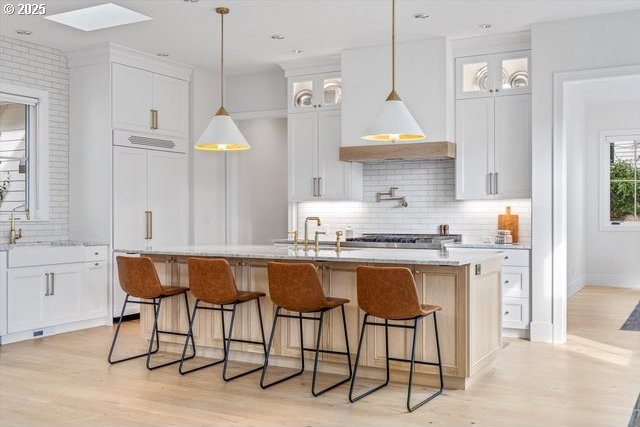 kitchen with a sink, backsplash, white cabinets, and glass insert cabinets