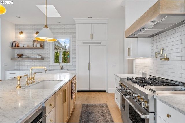 kitchen with high quality appliances, wall chimney exhaust hood, a sink, decorative backsplash, and light wood-style floors