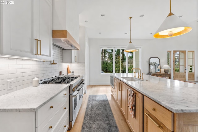kitchen featuring range with two ovens, a sink, light wood-type flooring, light stone counters, and backsplash