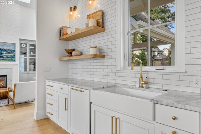 kitchen featuring open shelves, a sink, decorative backsplash, and light wood-style flooring