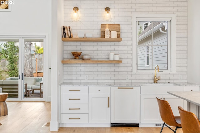 kitchen with light stone countertops, light wood-style flooring, open shelves, white cabinets, and backsplash