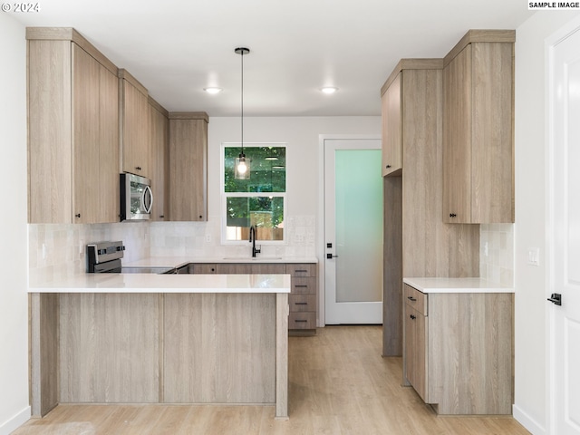 66 NE Stanton St, Portland, OR 97212 - kitchen with kitchen peninsula, appliances with stainless steel finishes, light brown cabinetry, hanging light fixtures, and sink